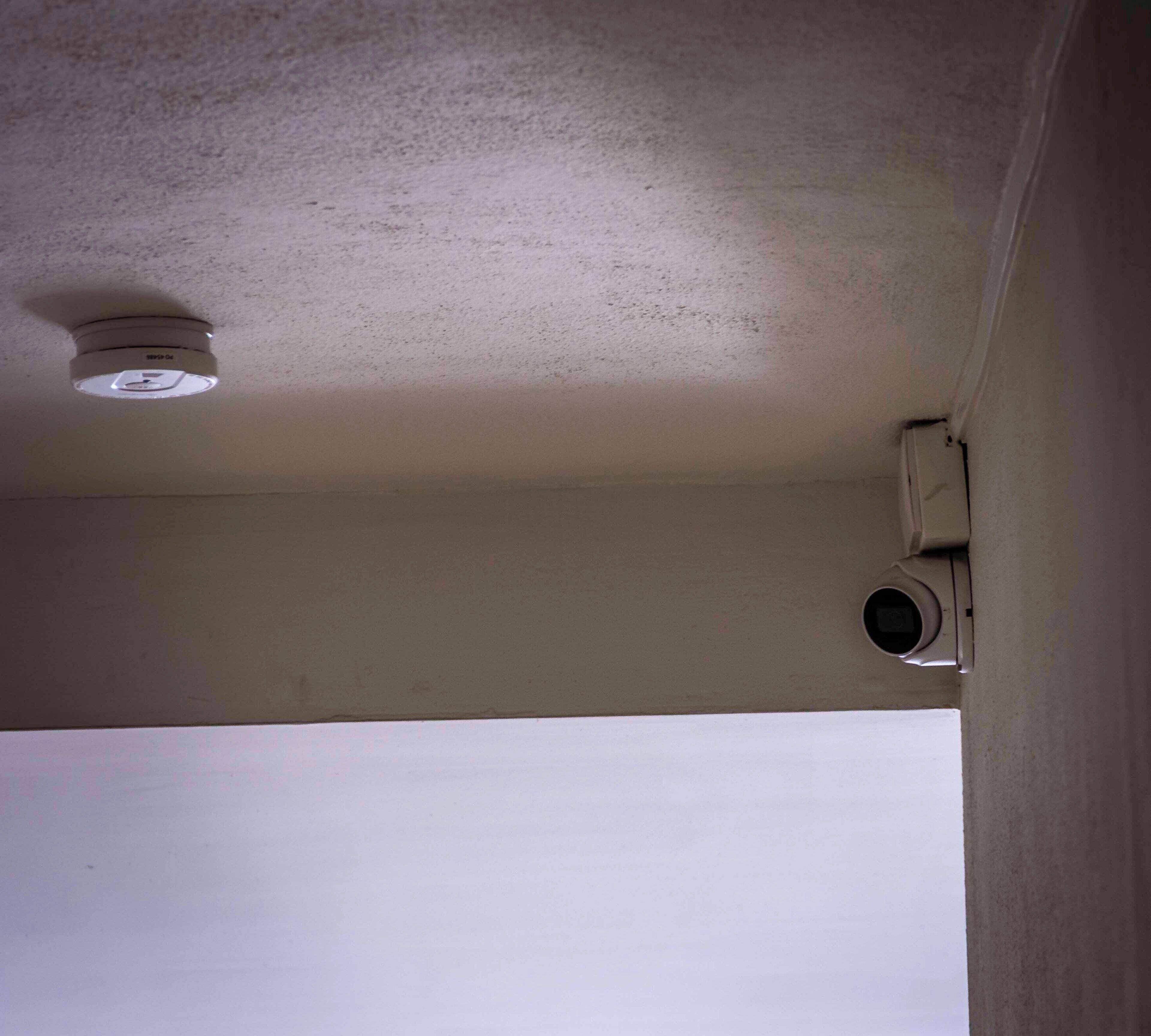 Un soffitto con un rilevatore di fumo e una griglia di aerazione a parete.