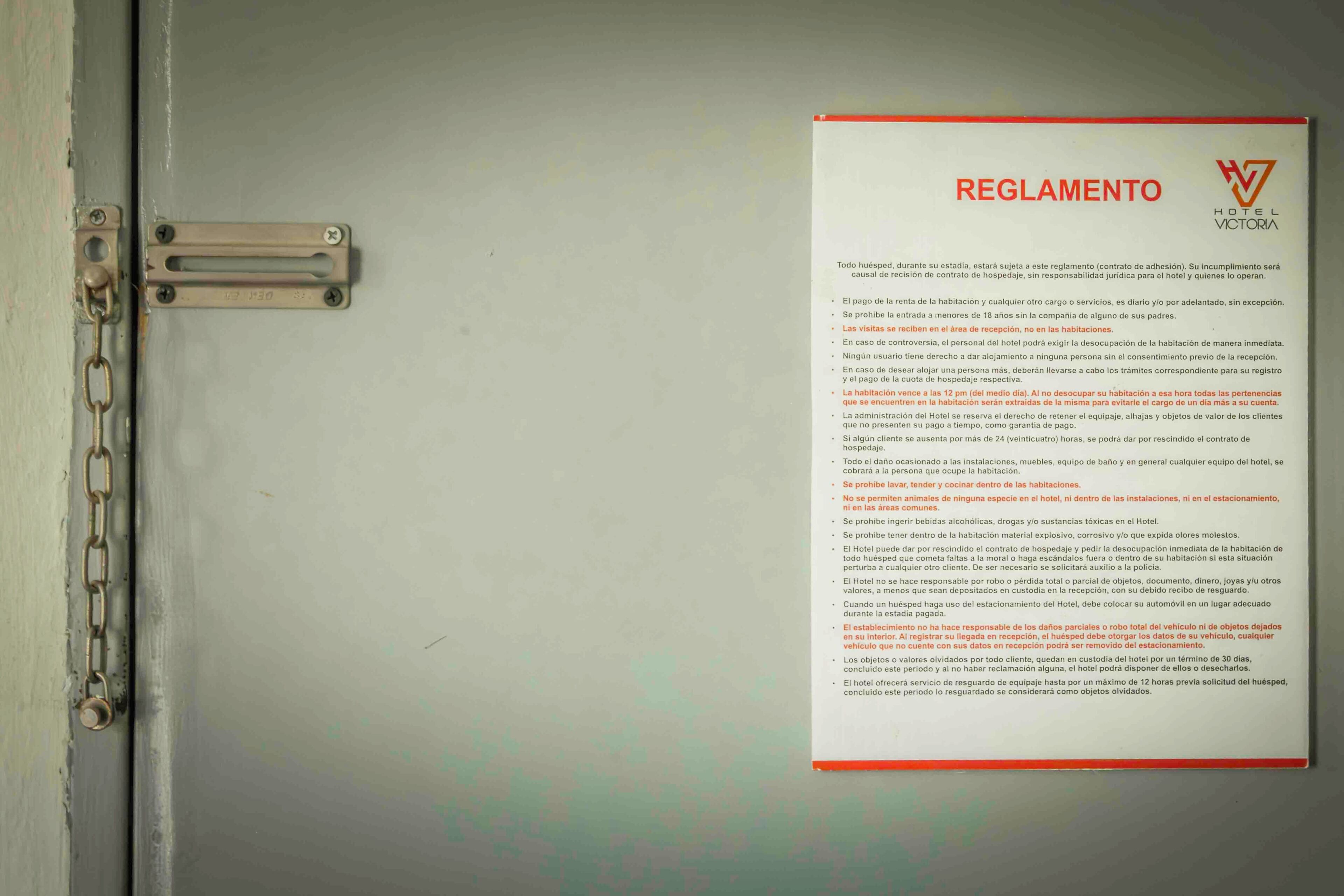 A hotel room door with a metal latch and a posted hotel rule sheet.