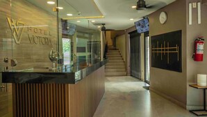 Ein Hotel-Empfangsbereich mit modernem Design, inklusive einer Rezeption, einer Treppe und einem Feuerlöscher.