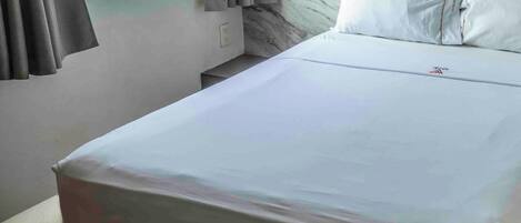 A neatly made bed with white linens, a marble headboard, and a window with curtains.
