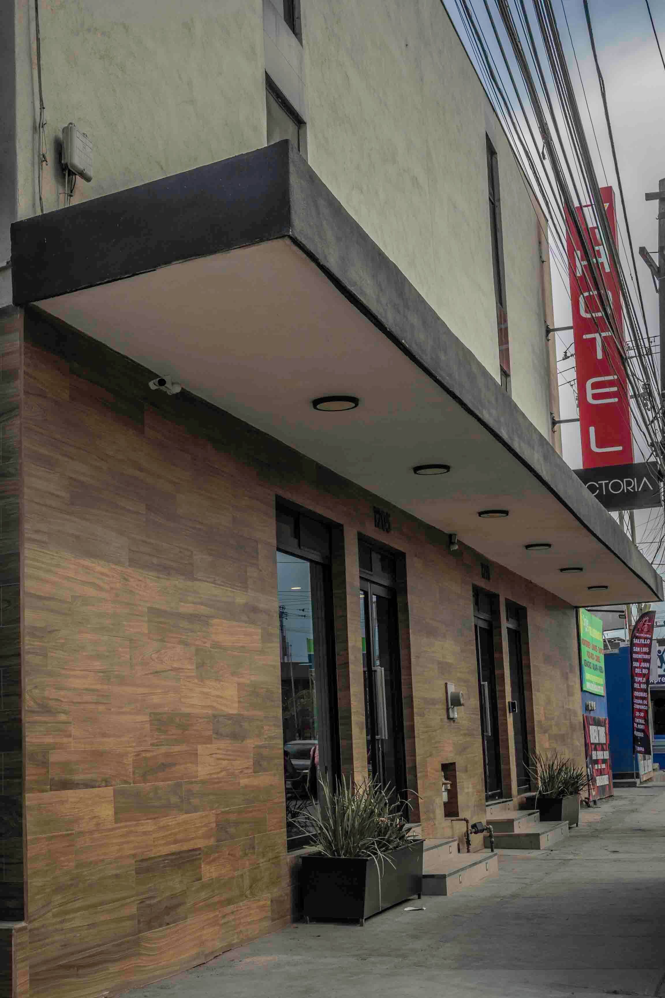 A hotel with a modern facade, a prominent red sign, and a series of windows.