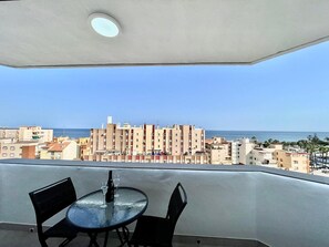 En balkong med ett bord och stolar, med utsikt över en kuststad med dess byggnader och havet.
