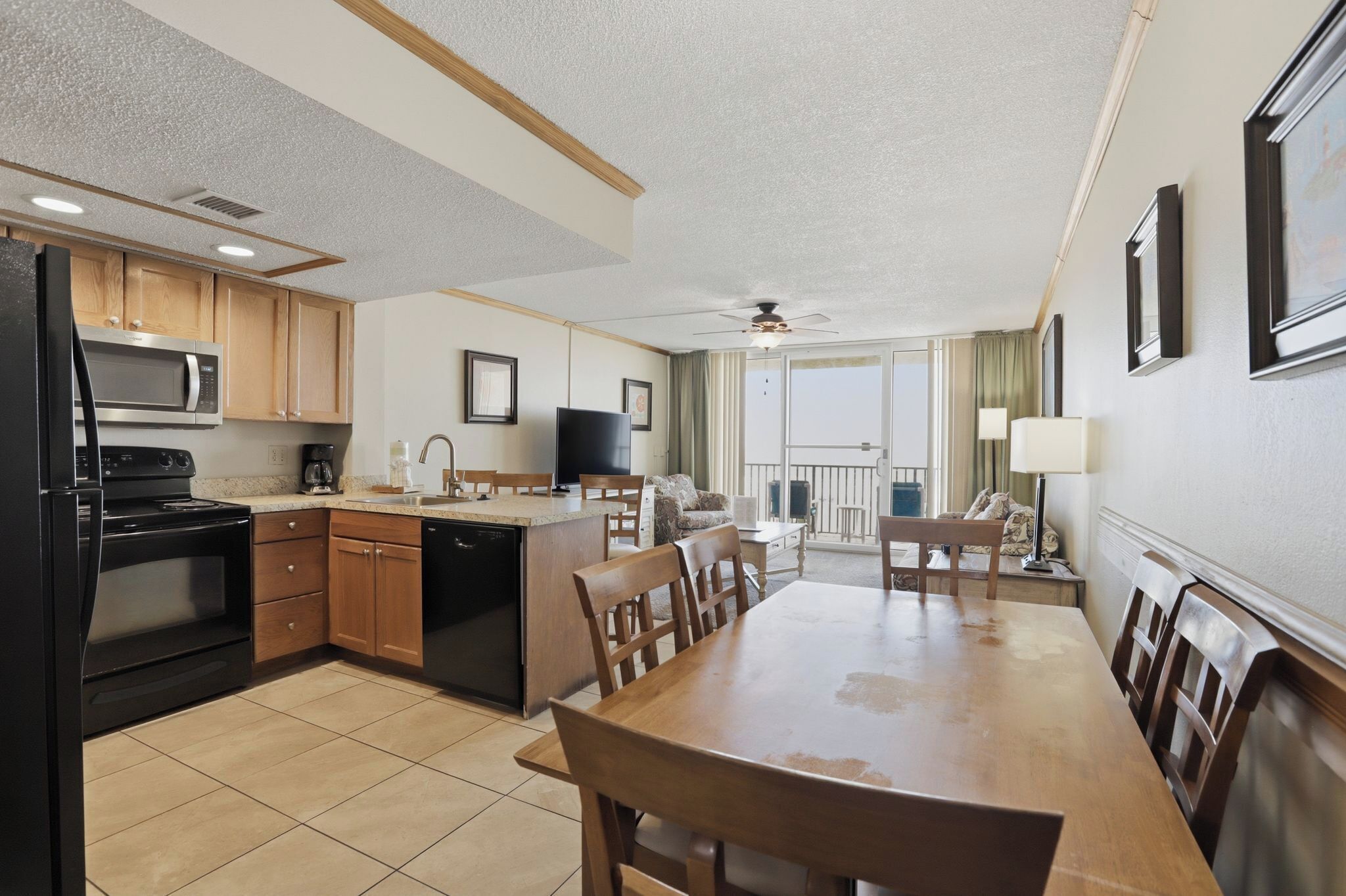 A modern kitchen with a dining area, wooden cabinets, a microwave, and a television.