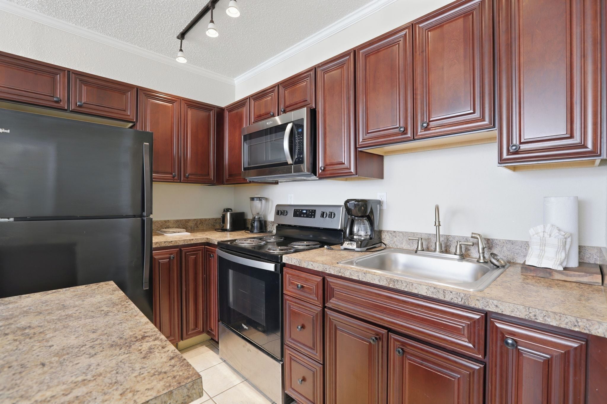 A kitchen with wooden cabinets, a stainless steel refrigerator, a microwave, a stove, and a sink.