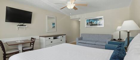 Habitación de hotel con cama, escritorio, silla, televisor, ventilador de techo y dos sillones.