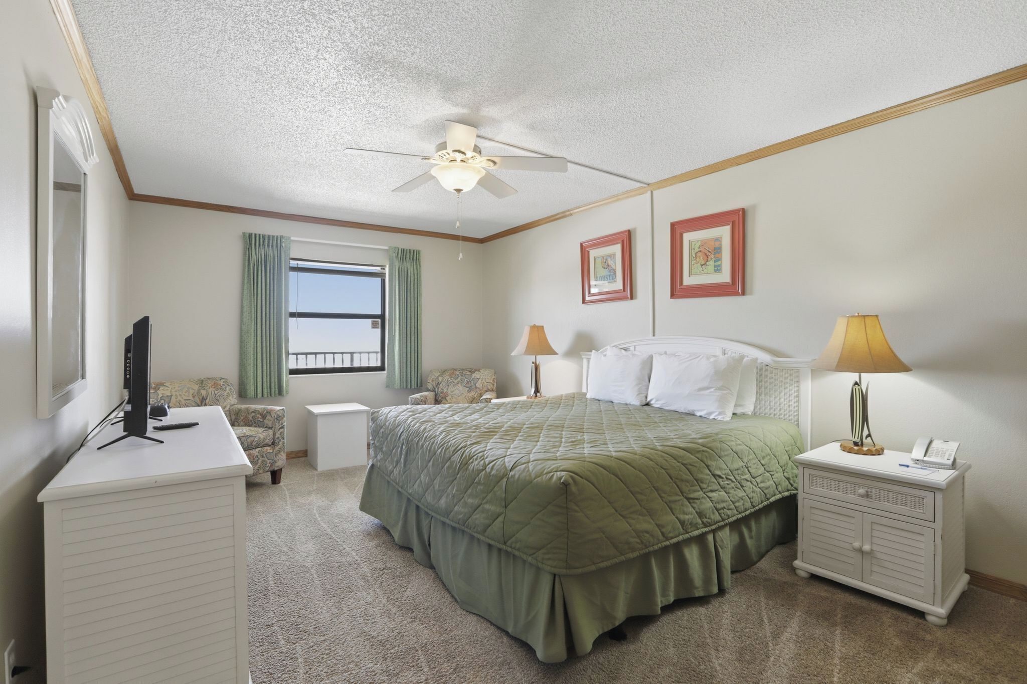 A bedroom with a bed, a desk, a chair, a nightstand, a ceiling fan, and two framed pictures on the wall.