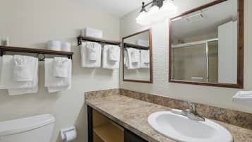 A bathroom with a sink, mirror, towel rack, toilet, and shower.