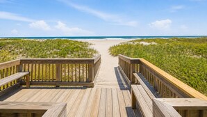Un paseo marítimo de madera que lleva a una playa con dunas y un cielo azul despejado.