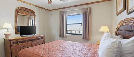 A hotel room with a bed, a television on a dresser, a ceiling fan, a window with curtains, and a view of the outside.