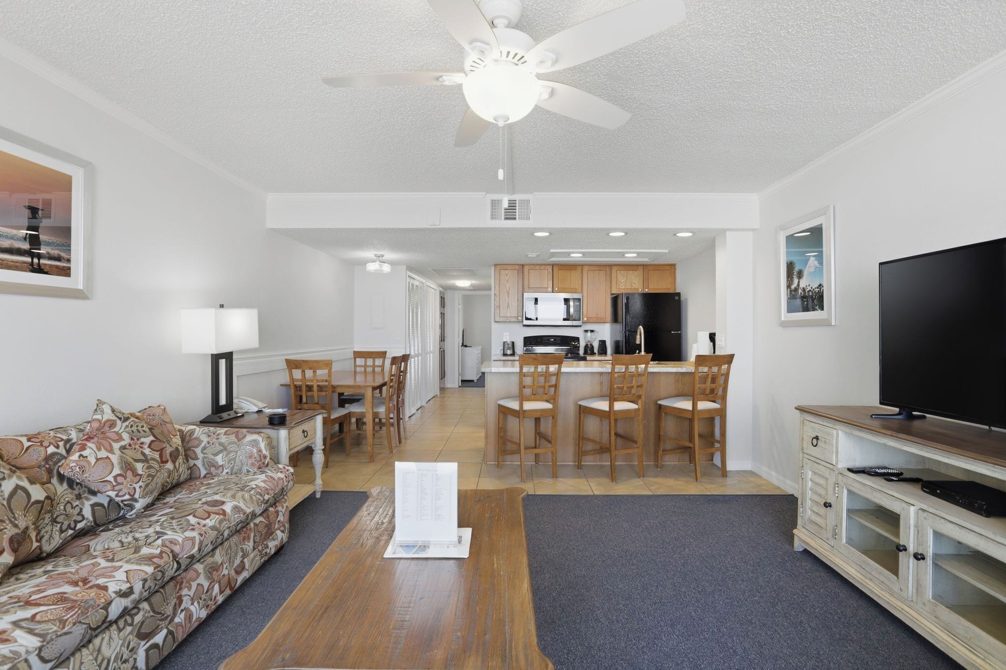 A living room with a sofa, a coffee table, a TV, and a kitchen area with a dining table and chairs.