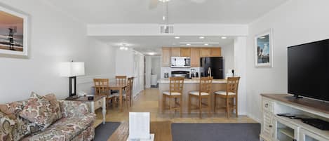 A living room with a sofa, a coffee table, a TV, and a kitchen area with a dining table and chairs.