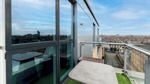 Un immeuble de grande hauteur doté de grandes fenêtres, d’un balcon offrant une vue sur la ville et d’un petit espace extérieur aménagé avec des sièges.