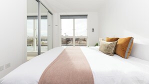 Une chambre moderne avec un grand lit, une vue sur un balcon extérieur accessible par une porte coulissante, et un luminaire au plafond.
