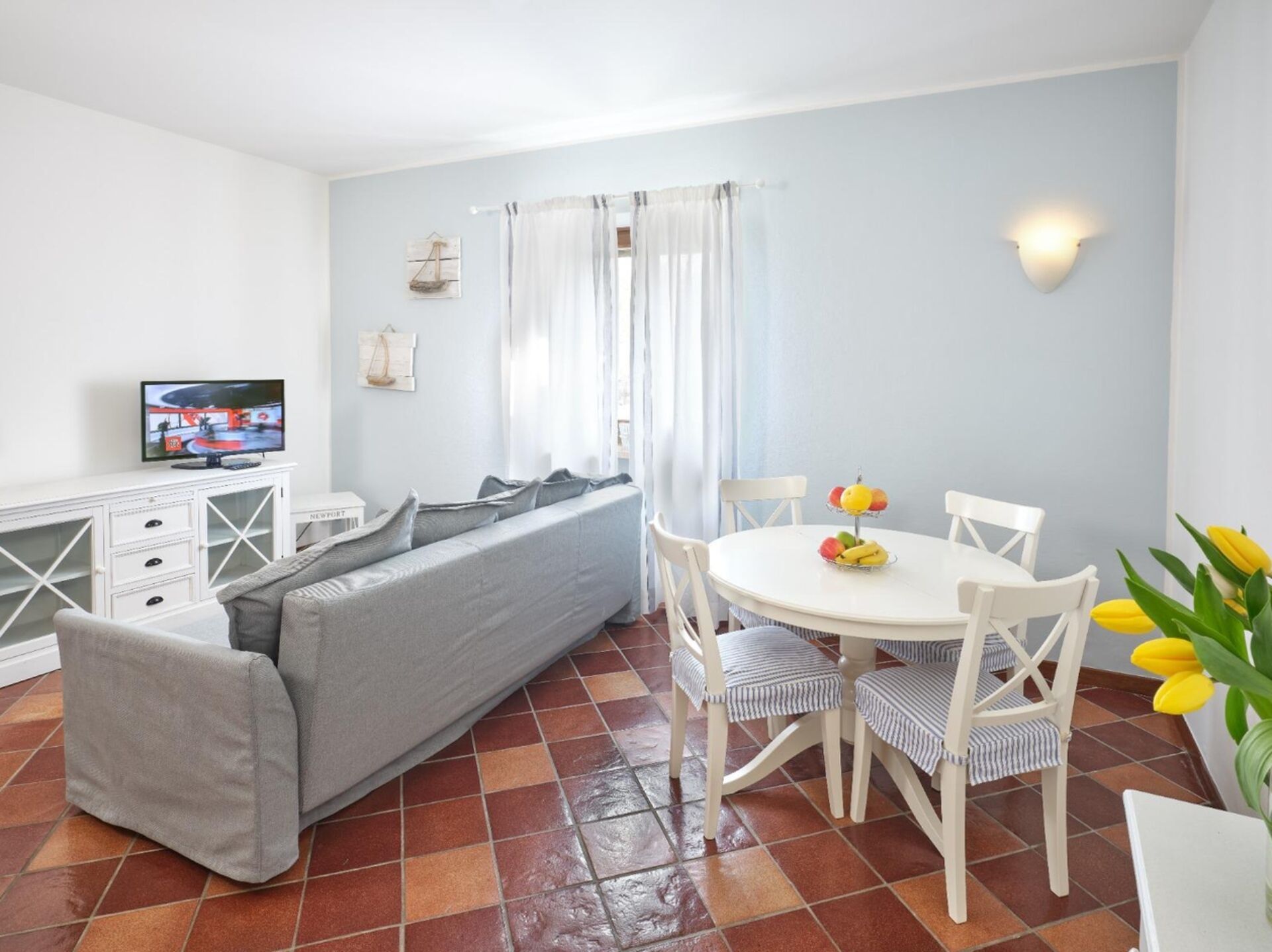 Een moderne woonkamer met een bank, een eettafel met stoelen, een televisietoestel en een raam met gordijnen.