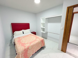 A bedroom with a bed, a nightstand, a wardrobe, and a door.