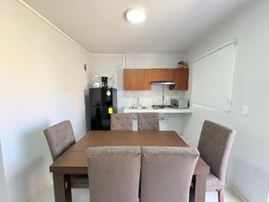 A compact kitchen with a black refrigerator, microwave, and gas stove. There is a dining table with four chairs and wooden cabinets above the counter.