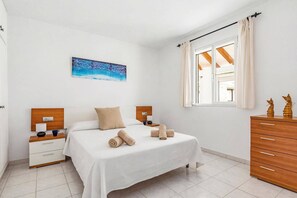 Ein Schlafzimmer mit Bett, Nachttischen, einem Schminktisch, einem Gemälde und einem Fenster mit Vorhängen.