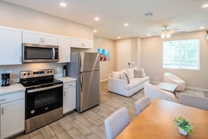 A modern kitchen with stainless steel appliances, a dining area with a wooden table and chairs, and a living area with a sofa and a ceiling fan. - The One Luxury Stay with Pool and Gym (Glendale)