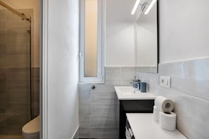 Een badkamer met een douche, een wastafel, een spiegel en toiletpapier.