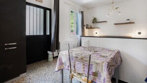 Ein Zimmer mit Tisch, Stühlen, einem dunklen Wandschrank, einem Fenster mit Vorhängen und einer Pendelleuchte.