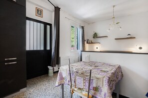 Een kamer met een tafel, stoelen, een donkere kast, een raam met gordijnen en een hanglamp.