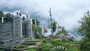 Um edifício de pedra com uma porta e degraus que conduzem a uma área rochosa com vegetação.