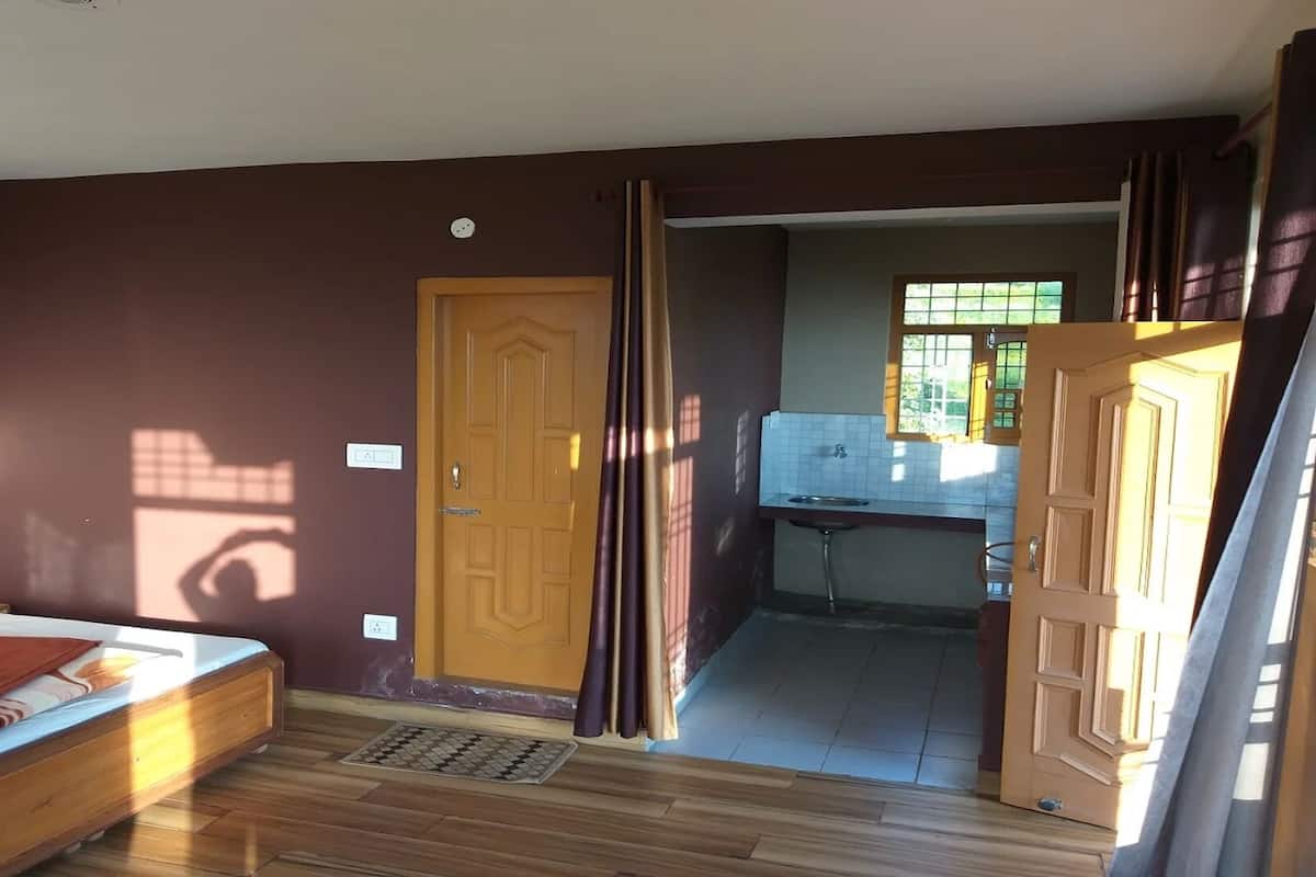 A room with a bed, a door leading to a kitchen, and a window.