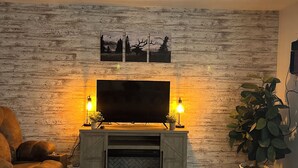 Una sala de estar con pared de madera, un televisor de pantalla plana, dos lámparas de pie, un sofá, una chimenea y una planta en maceta.