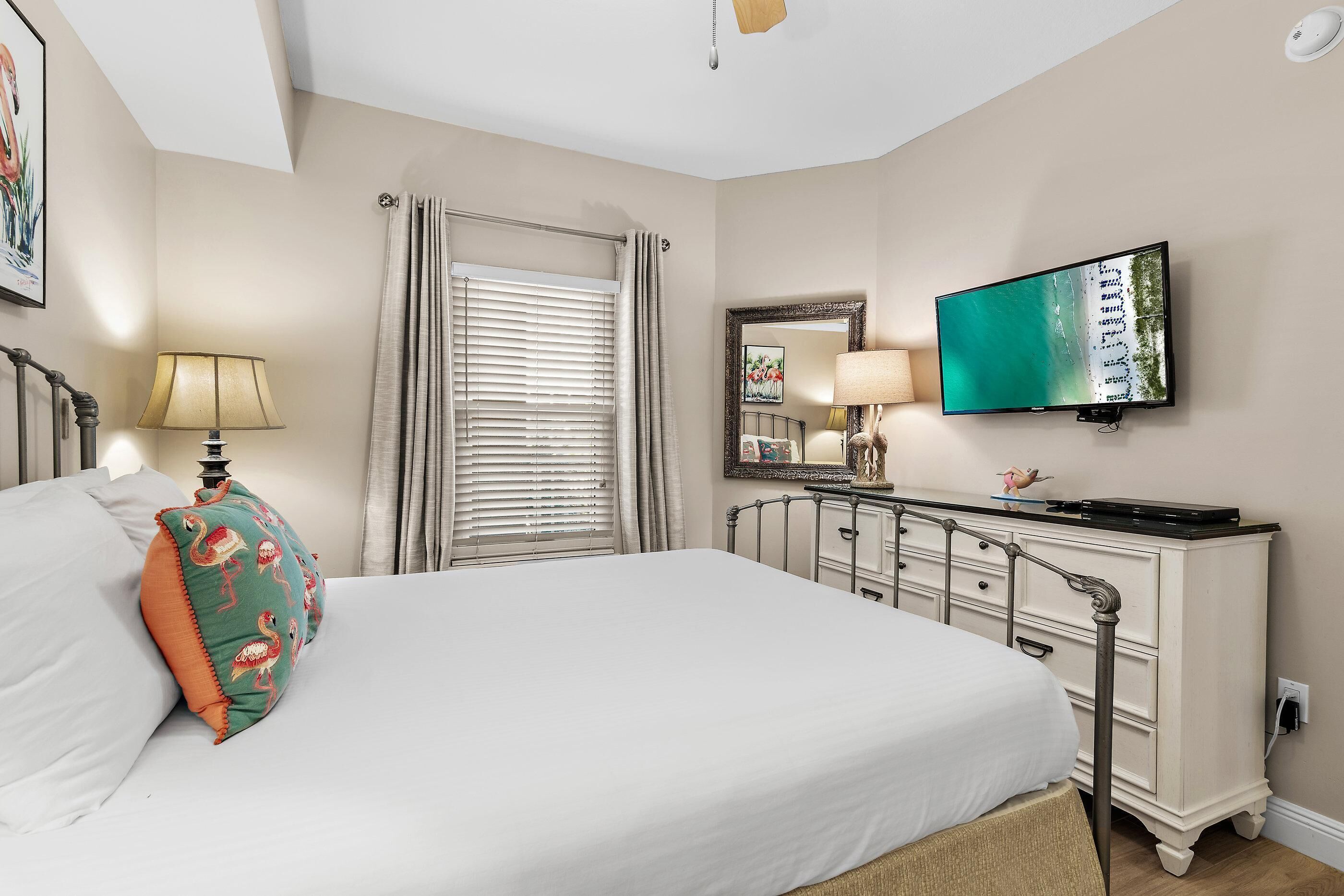 A bedroom with a bed, a dresser, a television, a window with curtains, and a lamp.