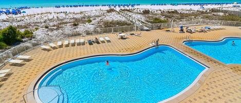 A pool area with two swimming pools, sun loungers, and a beach view.
