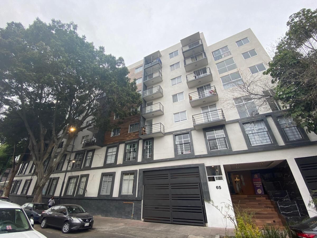 Un edificio residencial de varios pisos con balcones, un garaje y un árbol en la parte delantera.