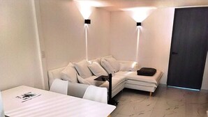 A modern living room with a white sofa, a small dining table, and two wall-mounted lights. - Apartment with modern design (Ciudad de México)