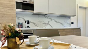 Une cuisine moderne avec des meubles blancs, un pare-feu en marbre et une machine à café posée sur le plan de travail.