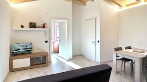 Un salon moderne avec un téléviseur, un coin repas avec une table et des chaises, et un couloir menant à une autre pièce.