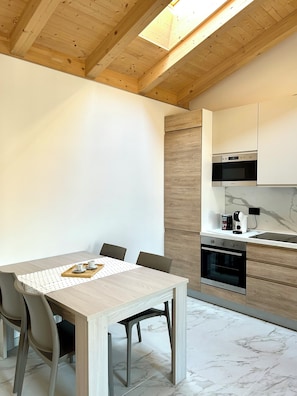 A modern kitchen with wooden beams, a dining table with chairs, and built-in appliances. - Apartment at the foot of the Castle and near Lake Garda (Sabbionara)