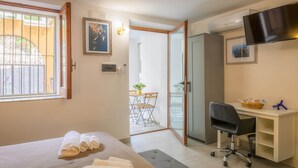 Et soveværelse med seng, skrivebord, stol, fjernsyn og en balkon.