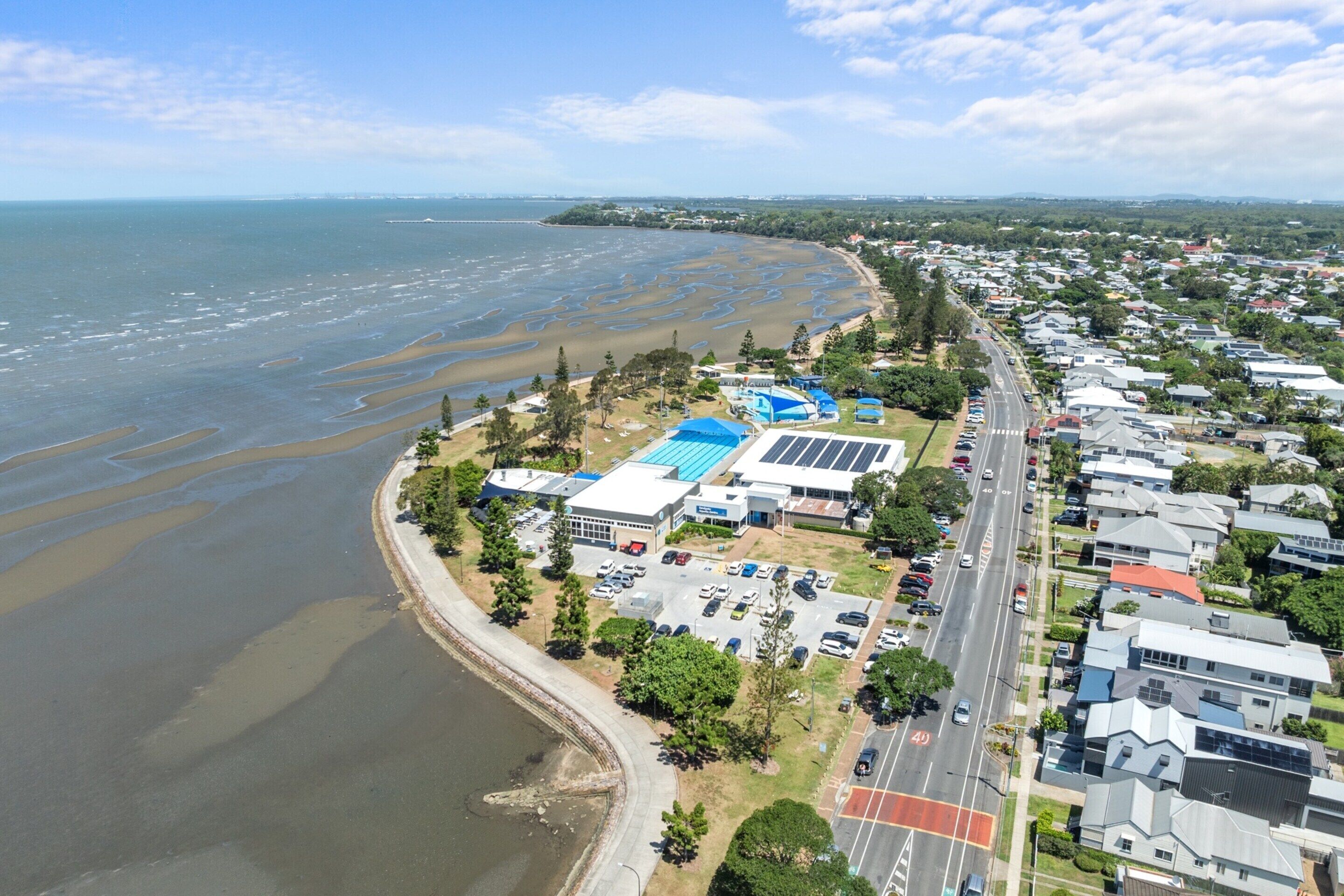An aerial view of a coastal residential area with houses, a beach, and a road.