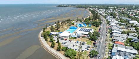 An aerial view of a coastal residential area with houses, a beach, and a road.