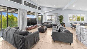 A spacious living area with a large TV, grey sofas, a dining table, and a kitchen island. - Family-sized Retreat With Private Garage (Brisbane)