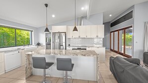 A modern kitchen with a large island, two bar stools, and pendant lighting. - Family-sized Retreat With Private Garage (Brisbane)