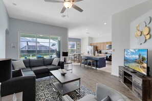 A modern living room with a sofa, coffee table, and TV. There is a kitchen area with a bar and a dining table. - Last Minute Disney Getaway! Private Pool, Hot Tub & Game Room. Book Now! #31454 (Orlando)