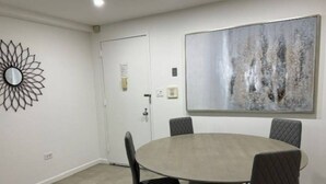 Een eethoek met een ronde tafel en vier stoelen, een deur en een abstract schilderij aan de muur.