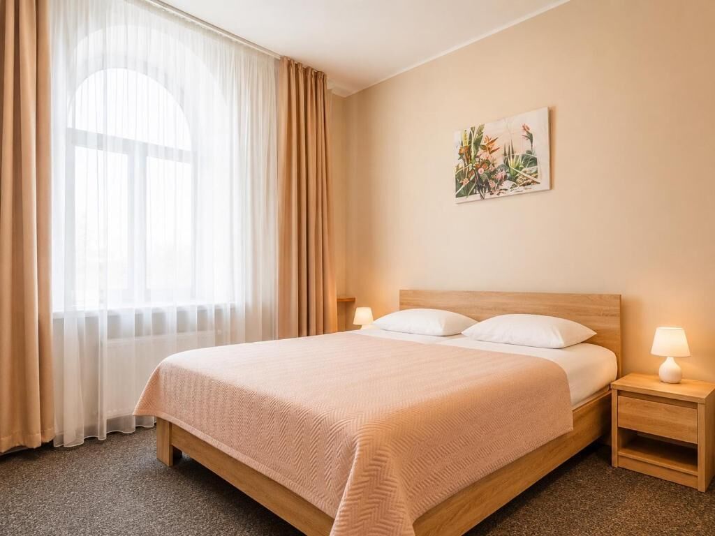 Et hotelværelse med en seng, et natbord, en lampe, et vindue med gardiner og et billede hængt på væggen.
