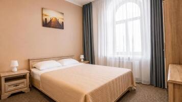 Hotellihuone, jossa on suuri sänky, yöpöytä, lamppu, seinällä taulu ja ikkuna, jossa on verhot.
