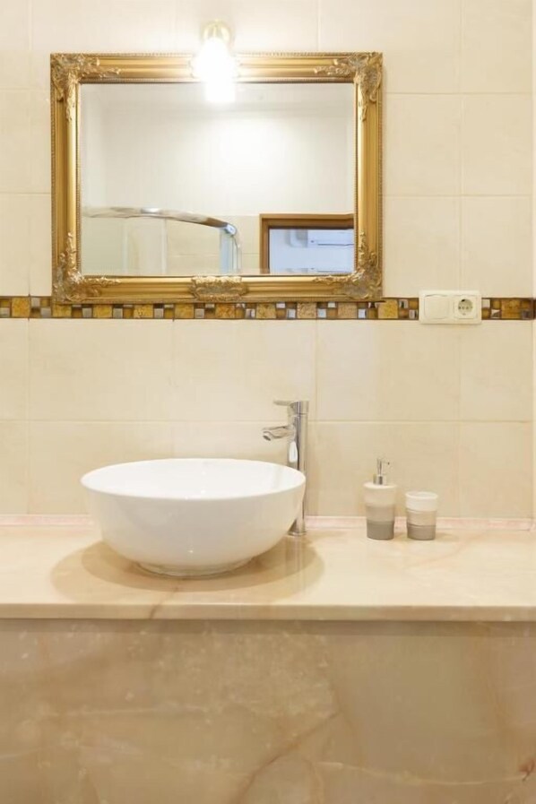 A bathroom with a large white vessel sink, a gold-framed mirror, and a tiled backsplash. - Nika Apart Hotel  (Riga)