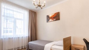 Un dormitorio con cama, mesita de noche, una silla, ventana con cortinas y un cuadro en la pared.