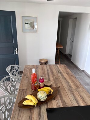 A dining area with a wooden table, white chairs, and a black electronic device. - Villa EKRIN (Bouillante)