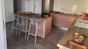 A modern kitchen with a central island, bar stools, a stainless steel refrigerator, and a wooden countertop. - Villa EKRIN (Bouillante)