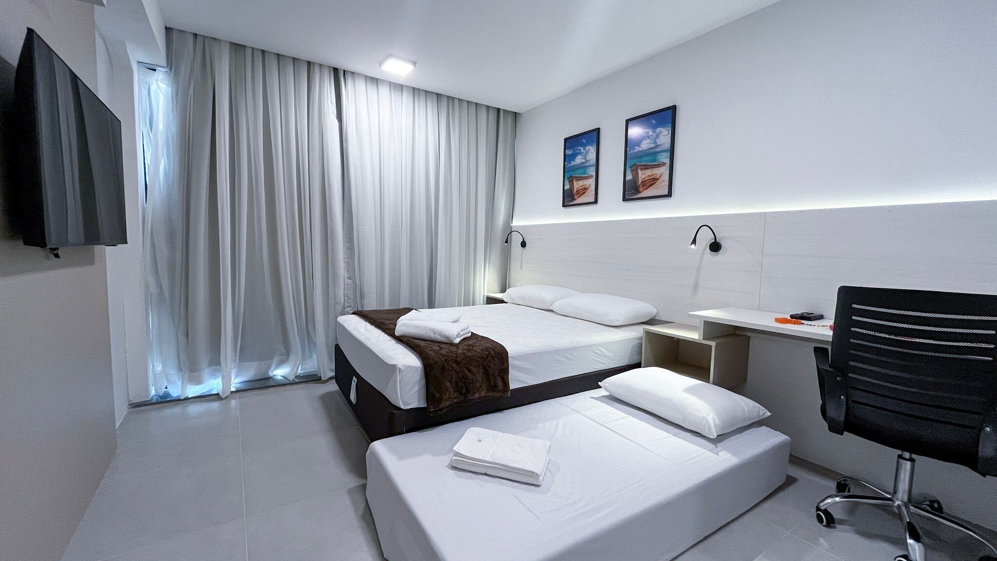Een hotelkamer met twee bedden, een bureau, een stoel, een televisie en een raam met gordijnen.