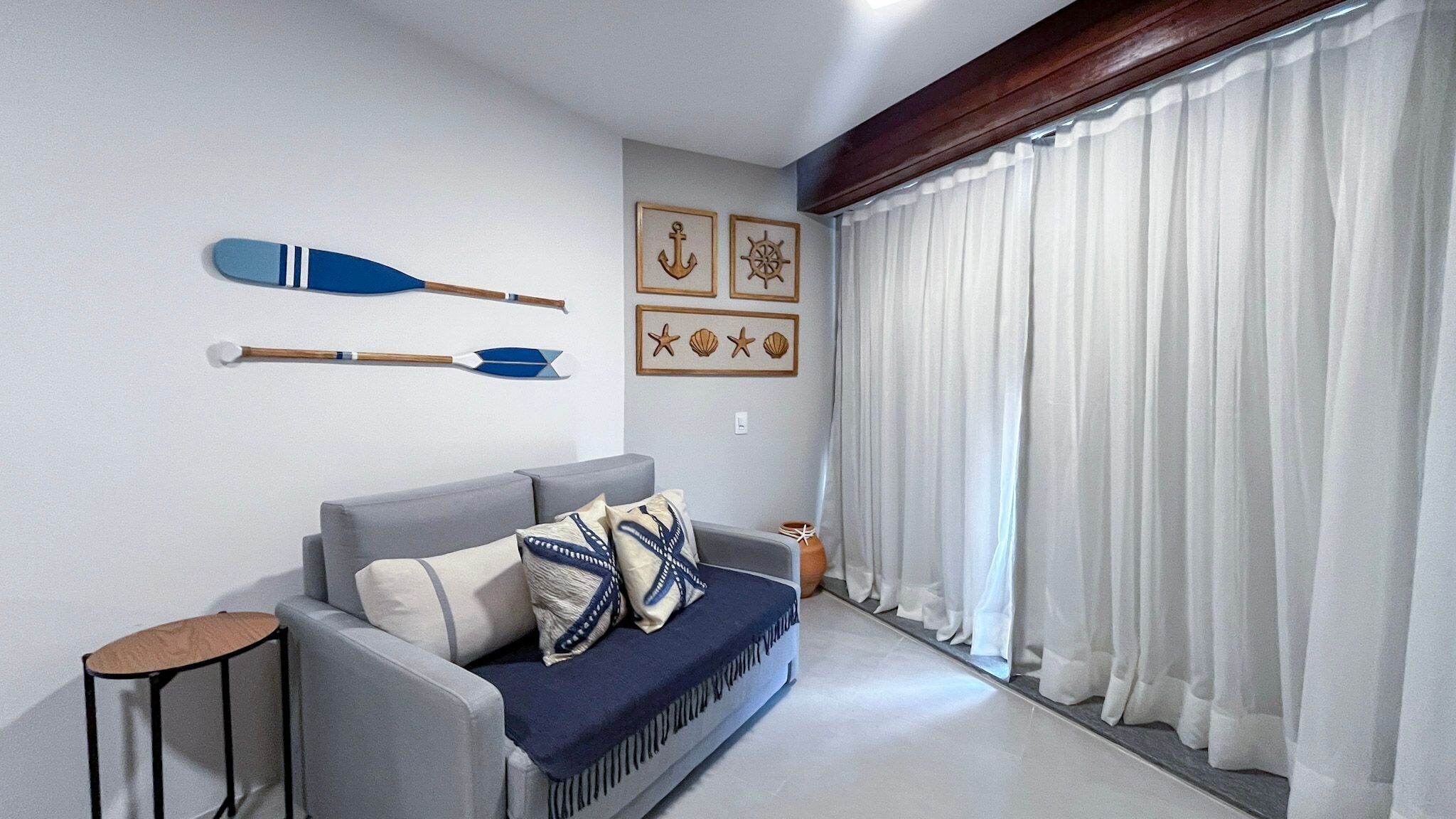 A living room with a grey sofa, decorative wall art, and a window with white curtains.